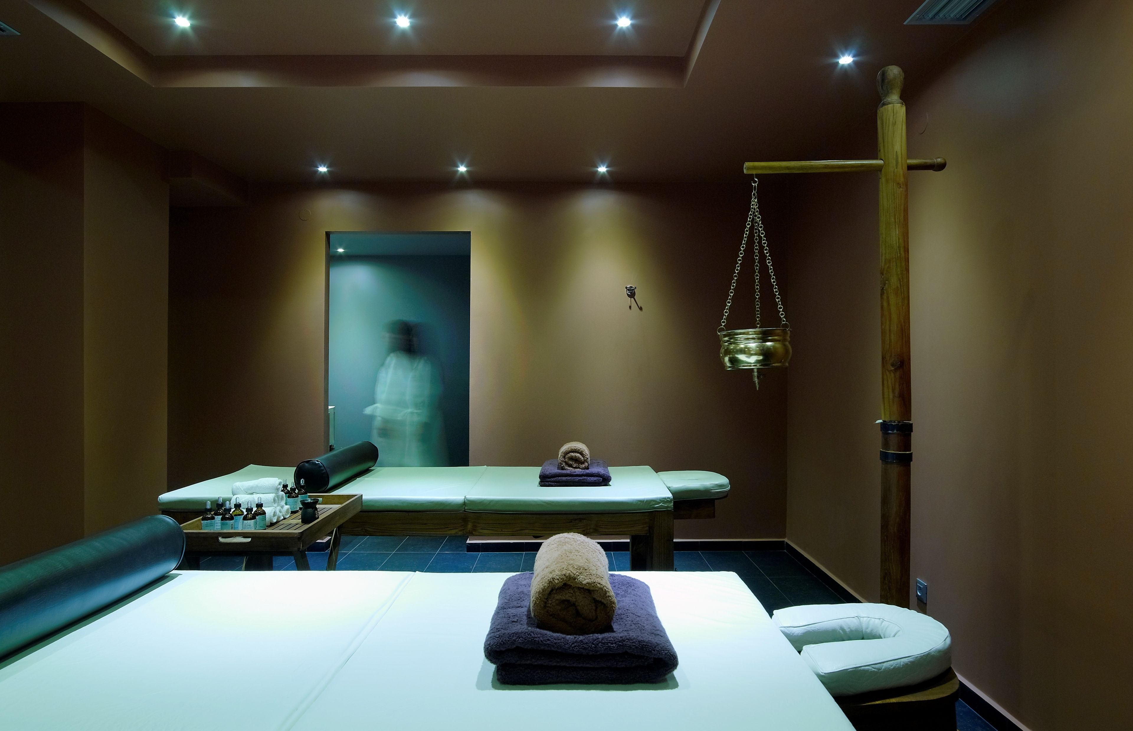 Een spa-ruimte met een massagetafel, een houten massagetafel, een metalen hangcontainer en een bank.
