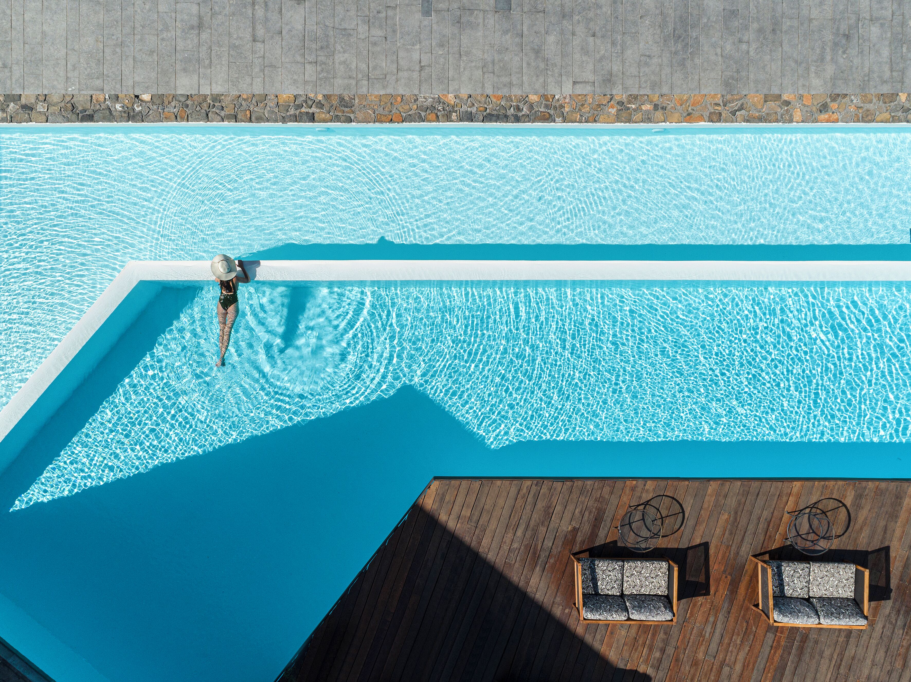 A swimming pool with a wooden deck area featuring two seating areas.