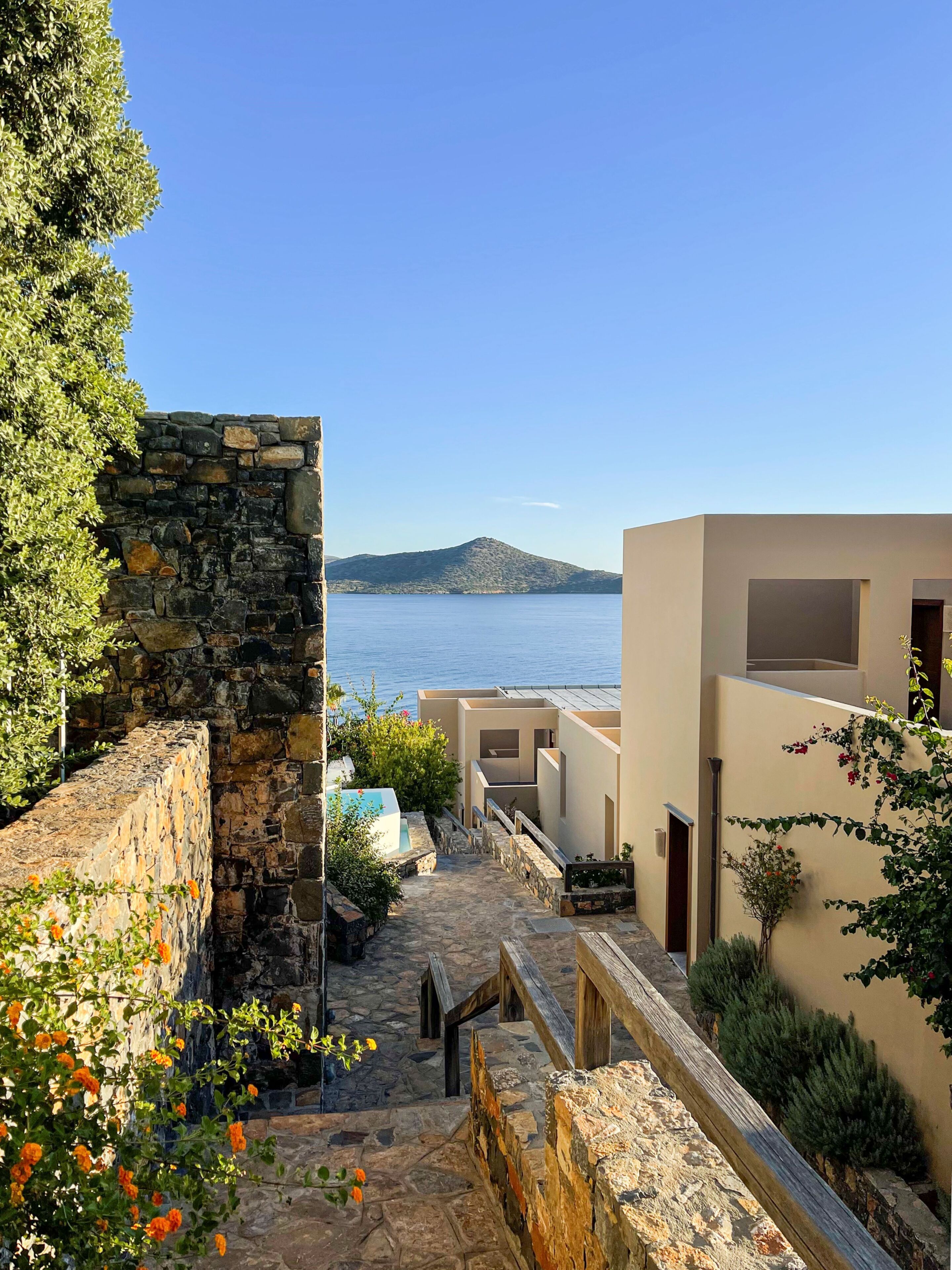 A narrow stone pathway leading to a building with a view of the sea and a distant island.