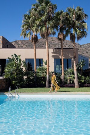 A pool area with palm trees, a clear sky, and a building with large windows.