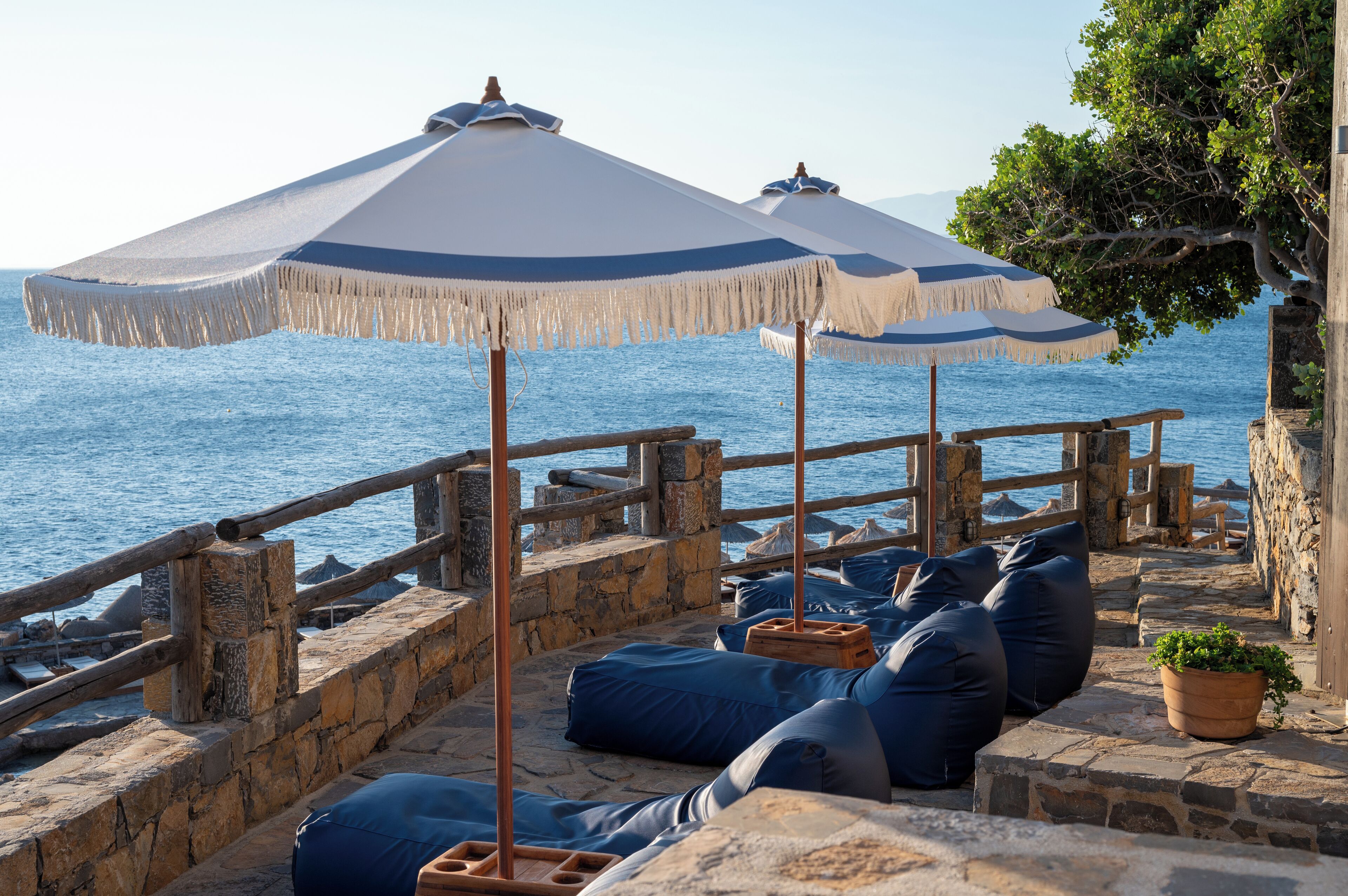 A stone deck with blue bean bags and umbrellas overlooking the sea.