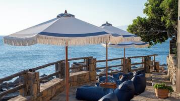 A stone deck with blue bean bags and umbrellas overlooking the sea.