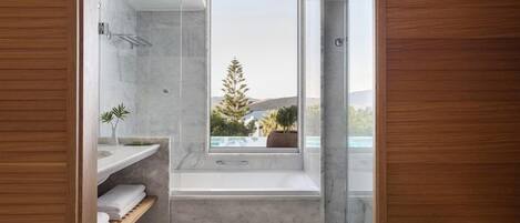 A modern bathroom with a glass shower enclosure, a built-in bench, and a window overlooking a pool and landscape.