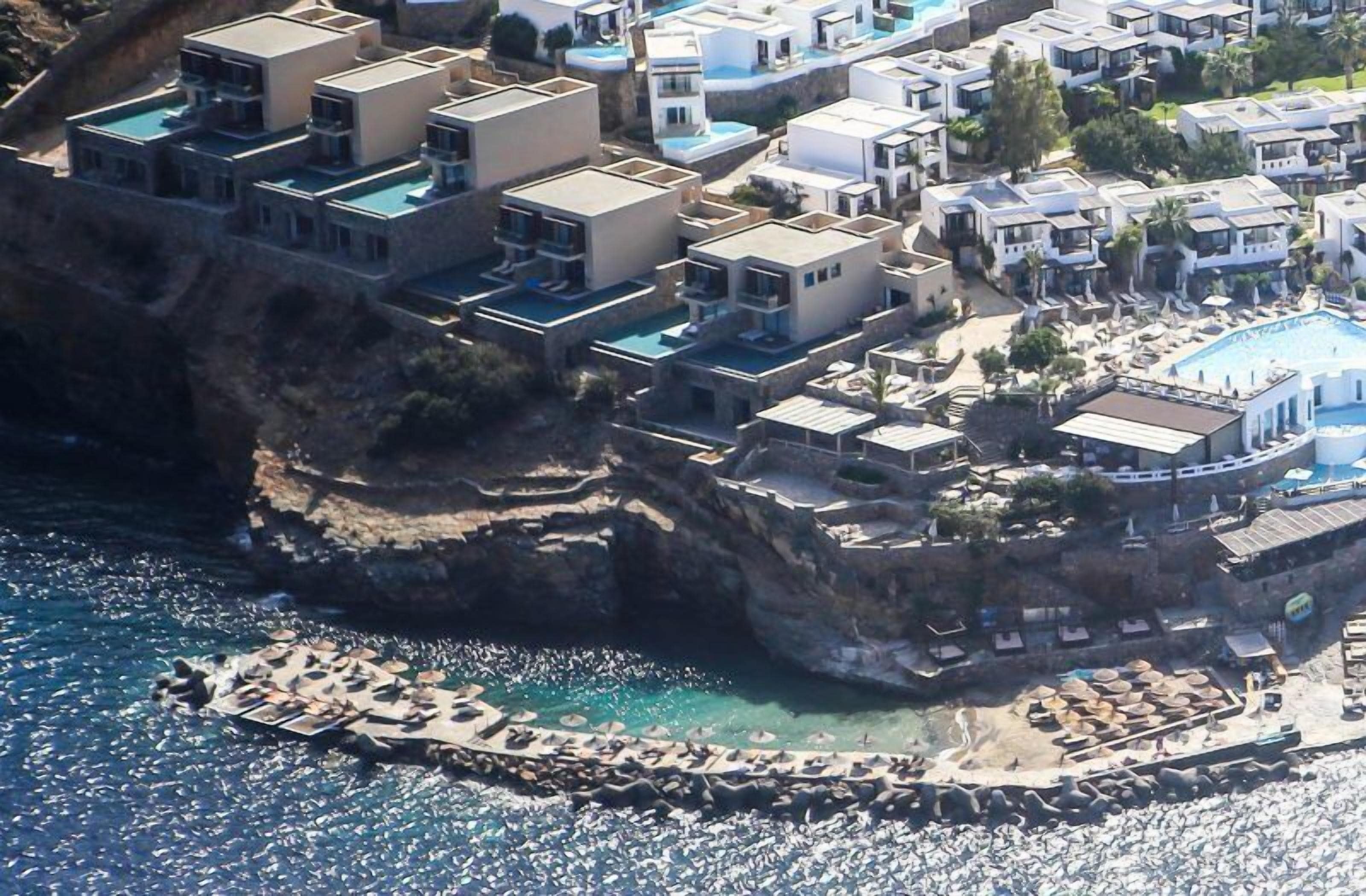 A coastal resort with modern buildings, a pool, and a rocky shoreline.