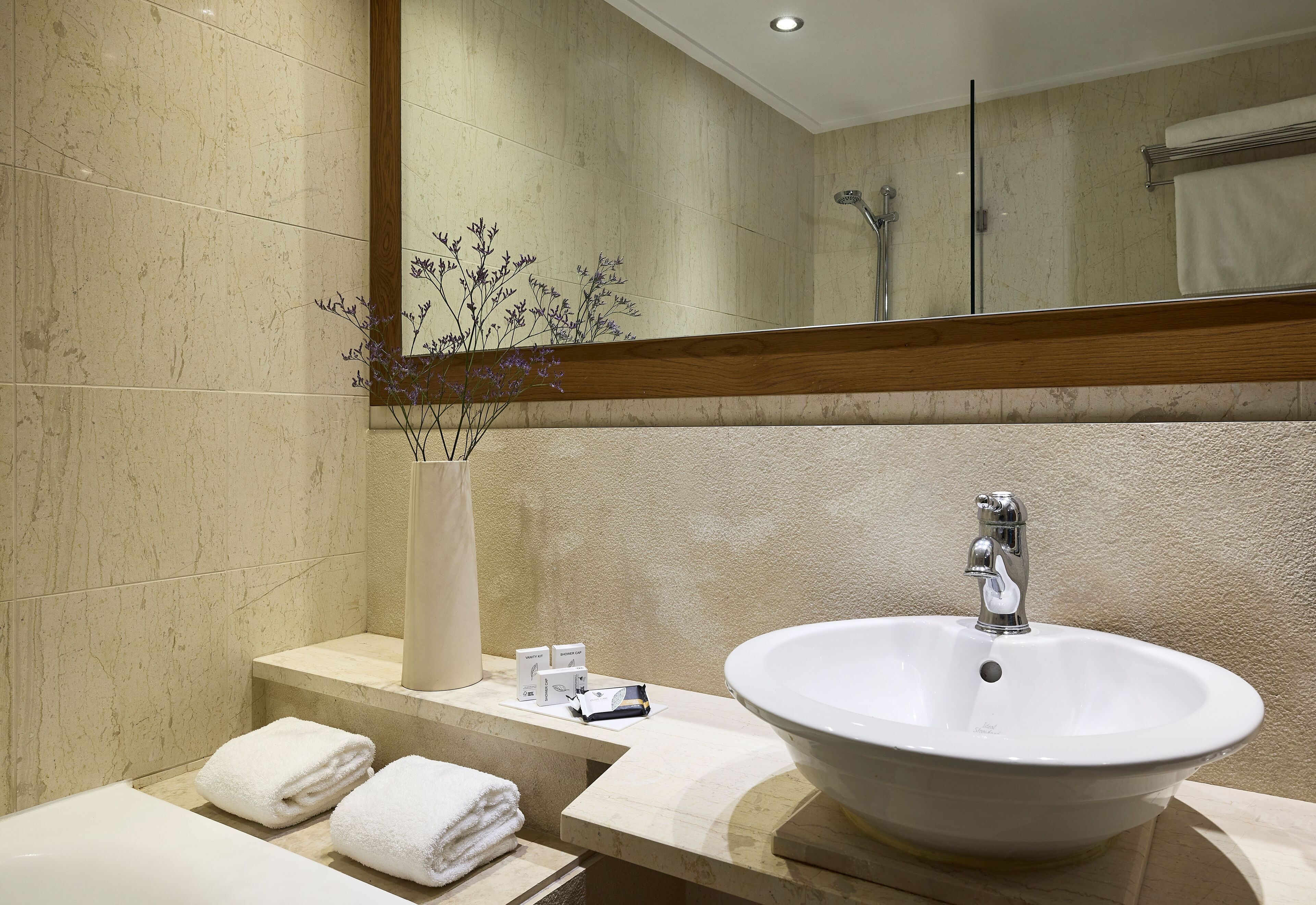 Un baño moderno con un lavamanos amplio, un espejo y un florero con flores.