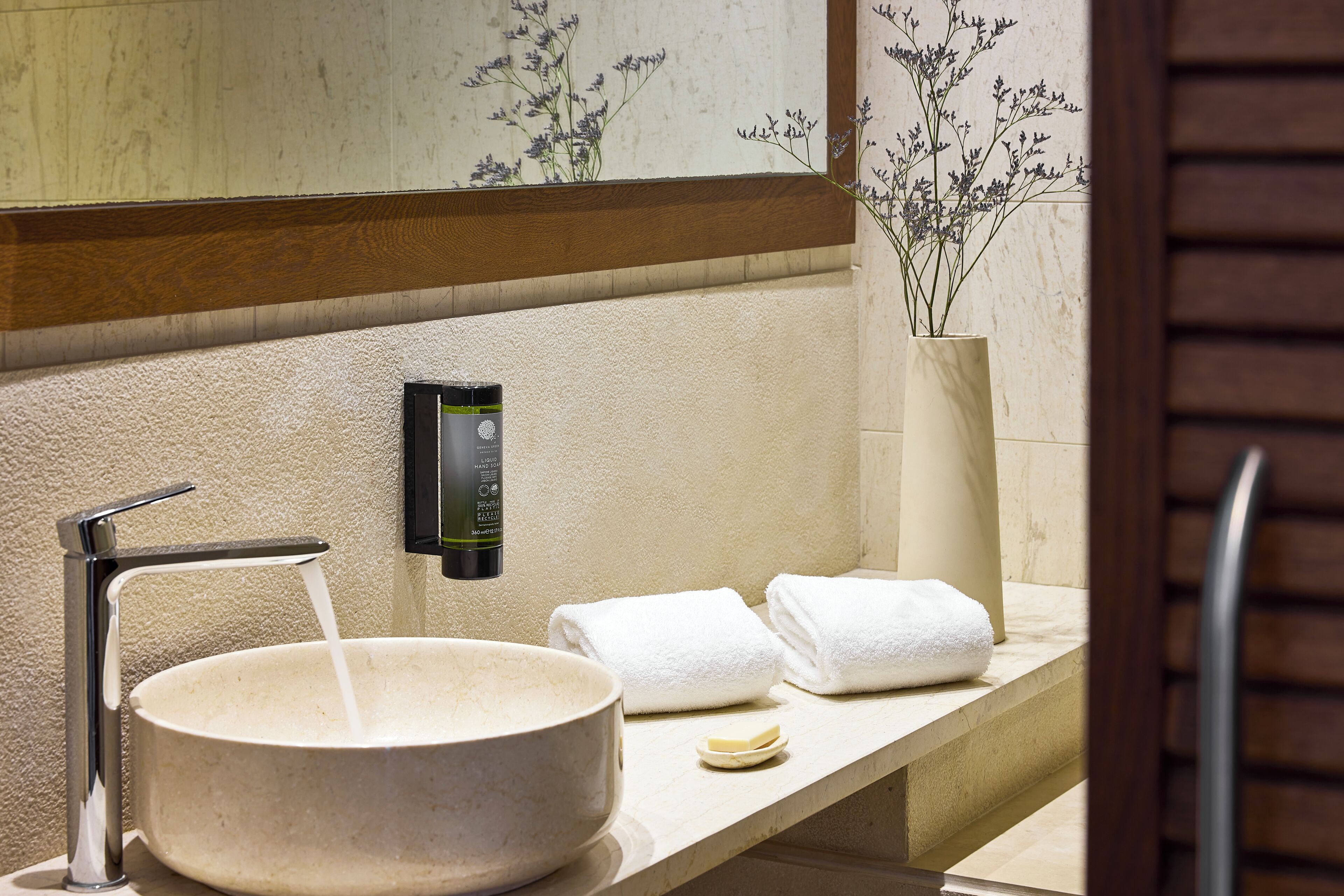 A bathroom with a large basin, a towel rack, and a soap dispenser.