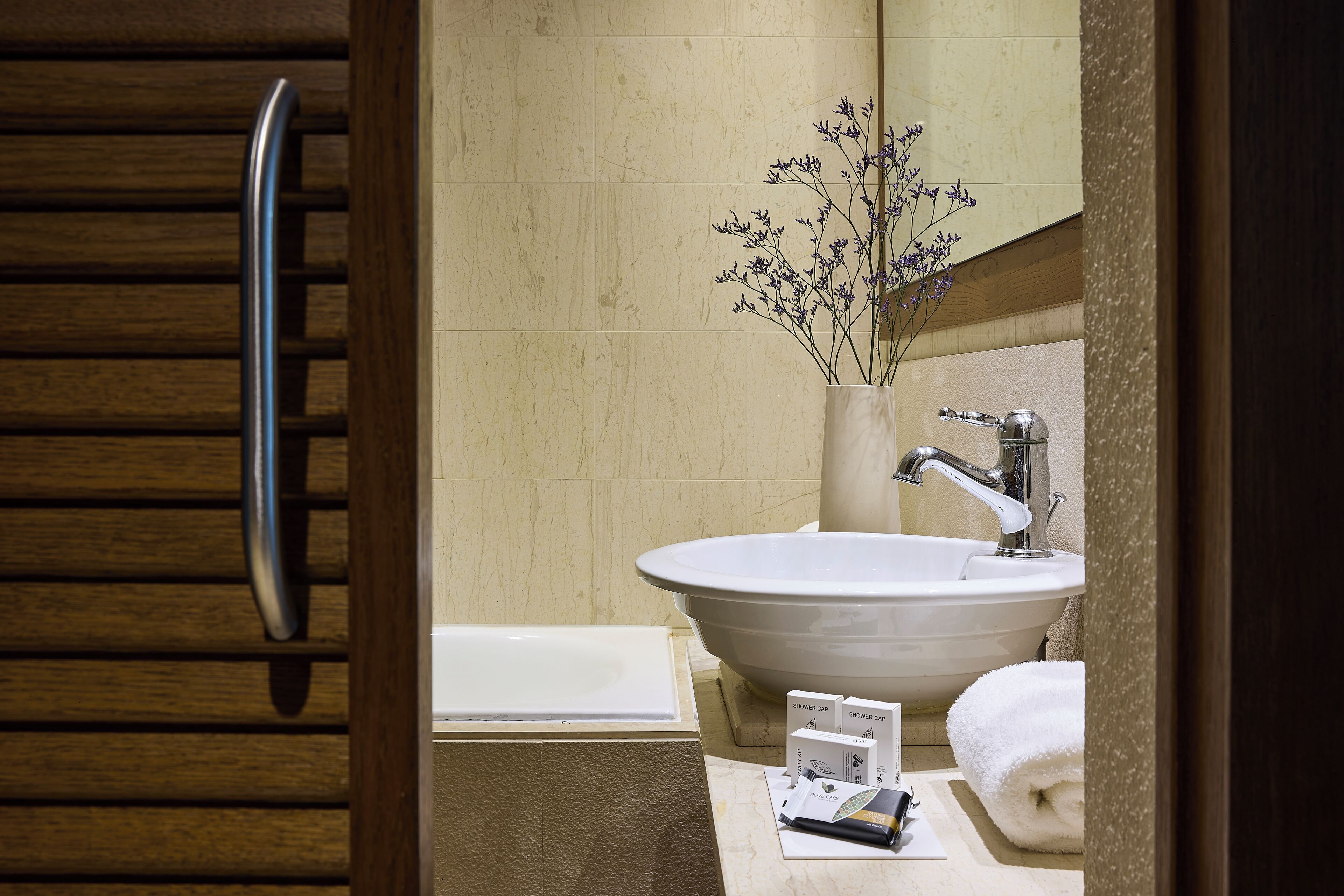 A bathroom with a large white sink, a mirror, a towel, and a shower cap on the counter.