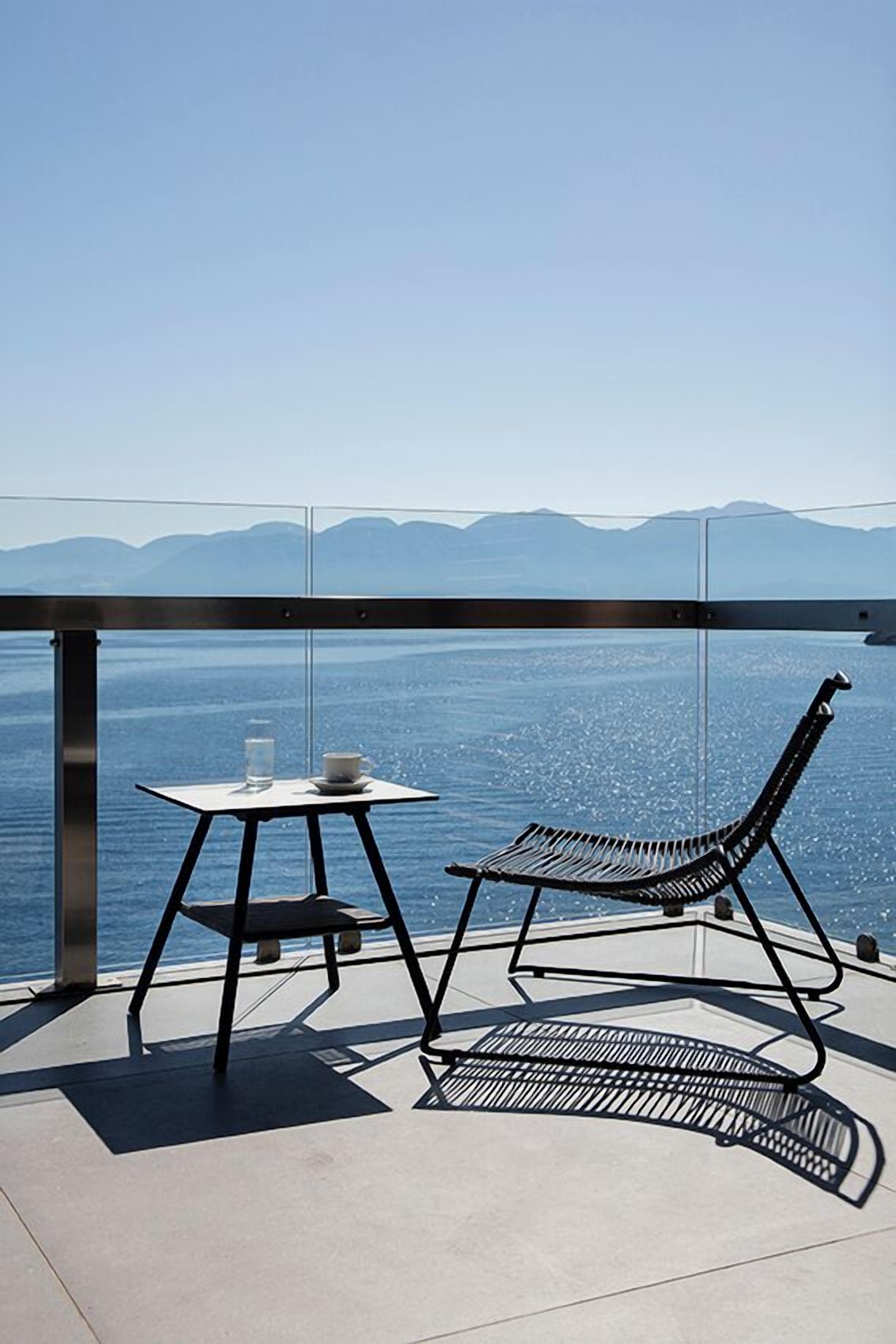 Varanda com mesa e cadeira, vista para um corpo d'água e montanhas ao longe.