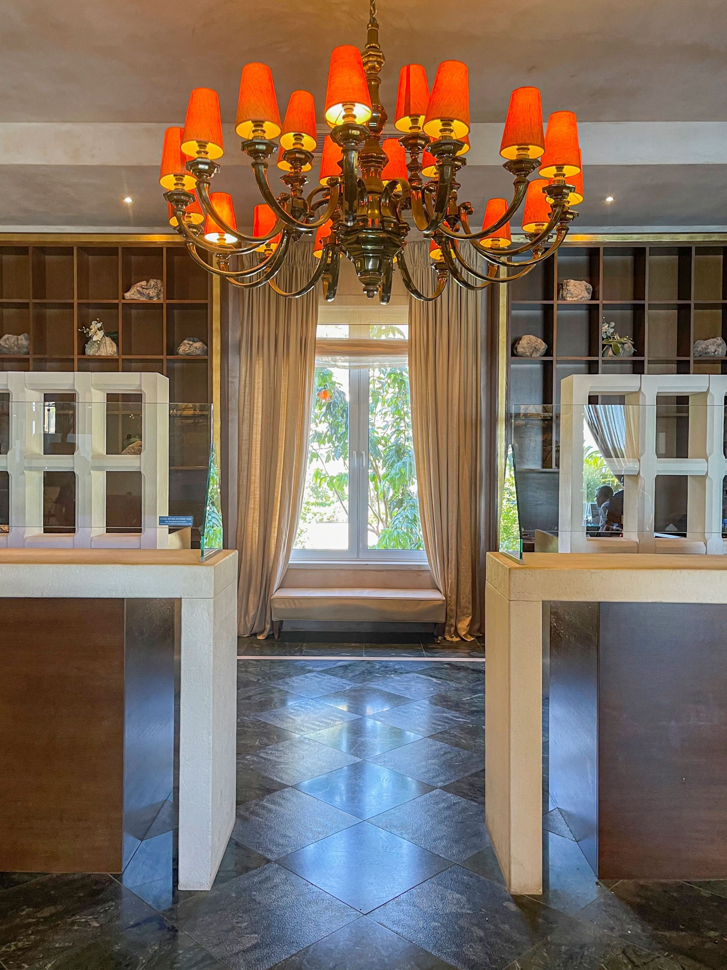 A lobby with a chandelier, a bench, and a view through a window.