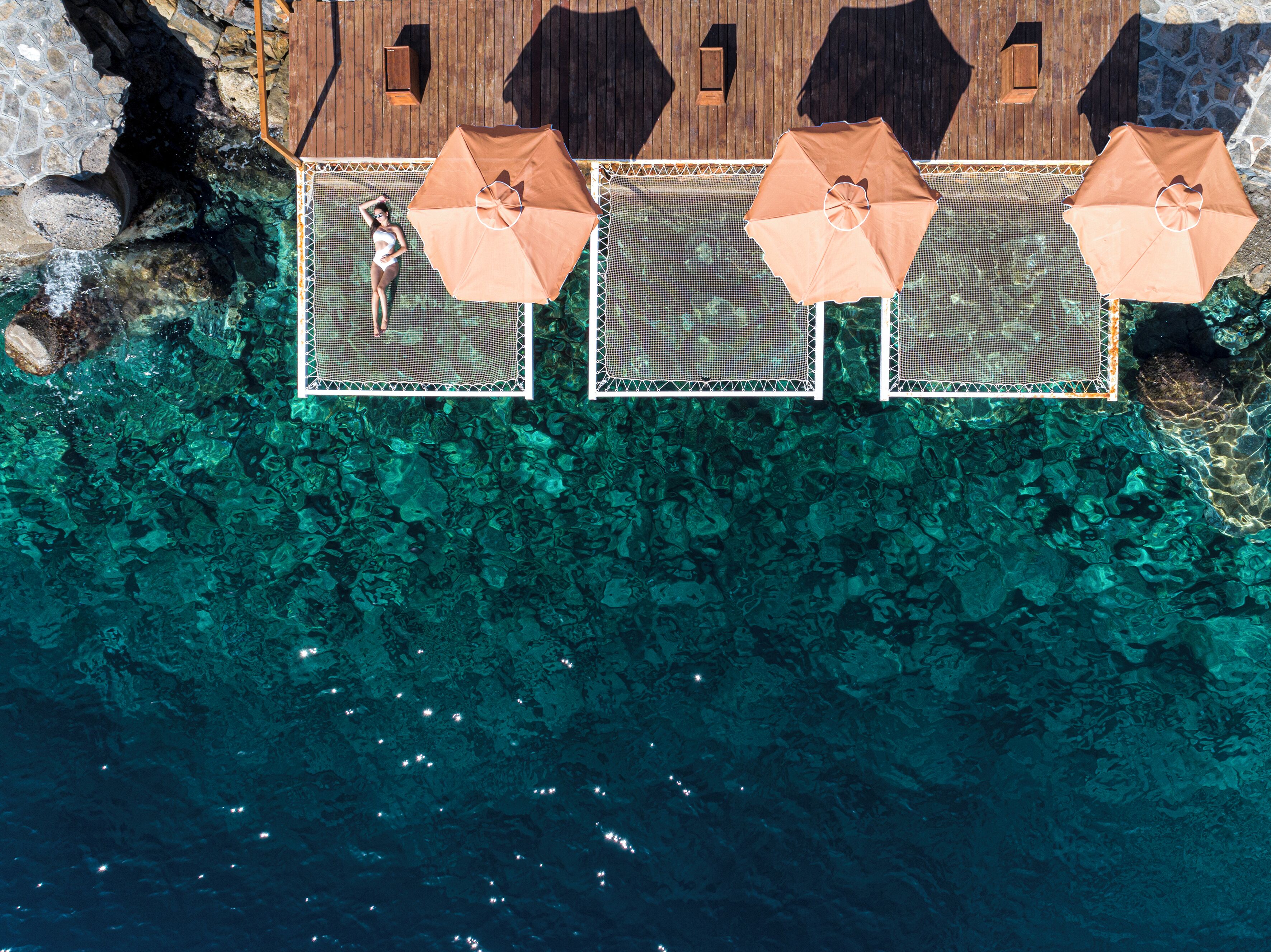 An aerial view of a beachside resort with clear turquoise waters, wooden deck, and umbrellas.
