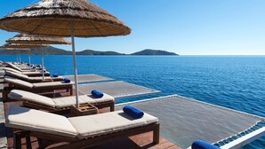 Une terrasse dotée de chaises longues en bois et de parasols en chaume, offrant une vue sur une mer calme.