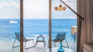 Un balcon avec deux chaises et une table, donnant sur une vaste étendue d’eau où l’on aperçoit un navire au loin.