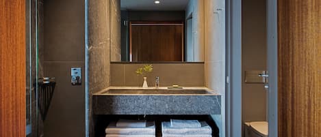 Un baño moderno con lavamanos de mármol, banco de madera y un espejo grande.