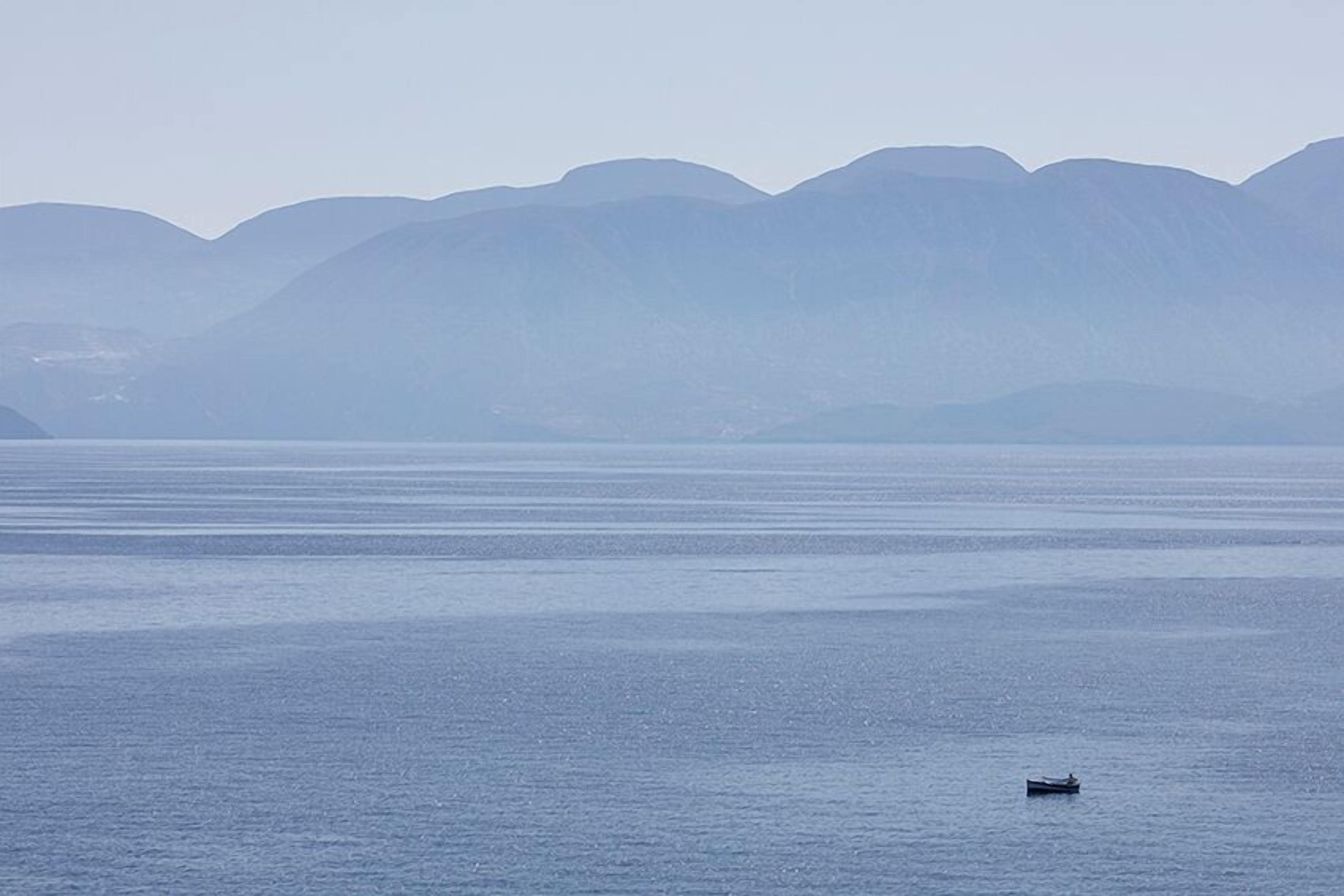 A calm body of water with a small boat in the distance and mountains in the background.