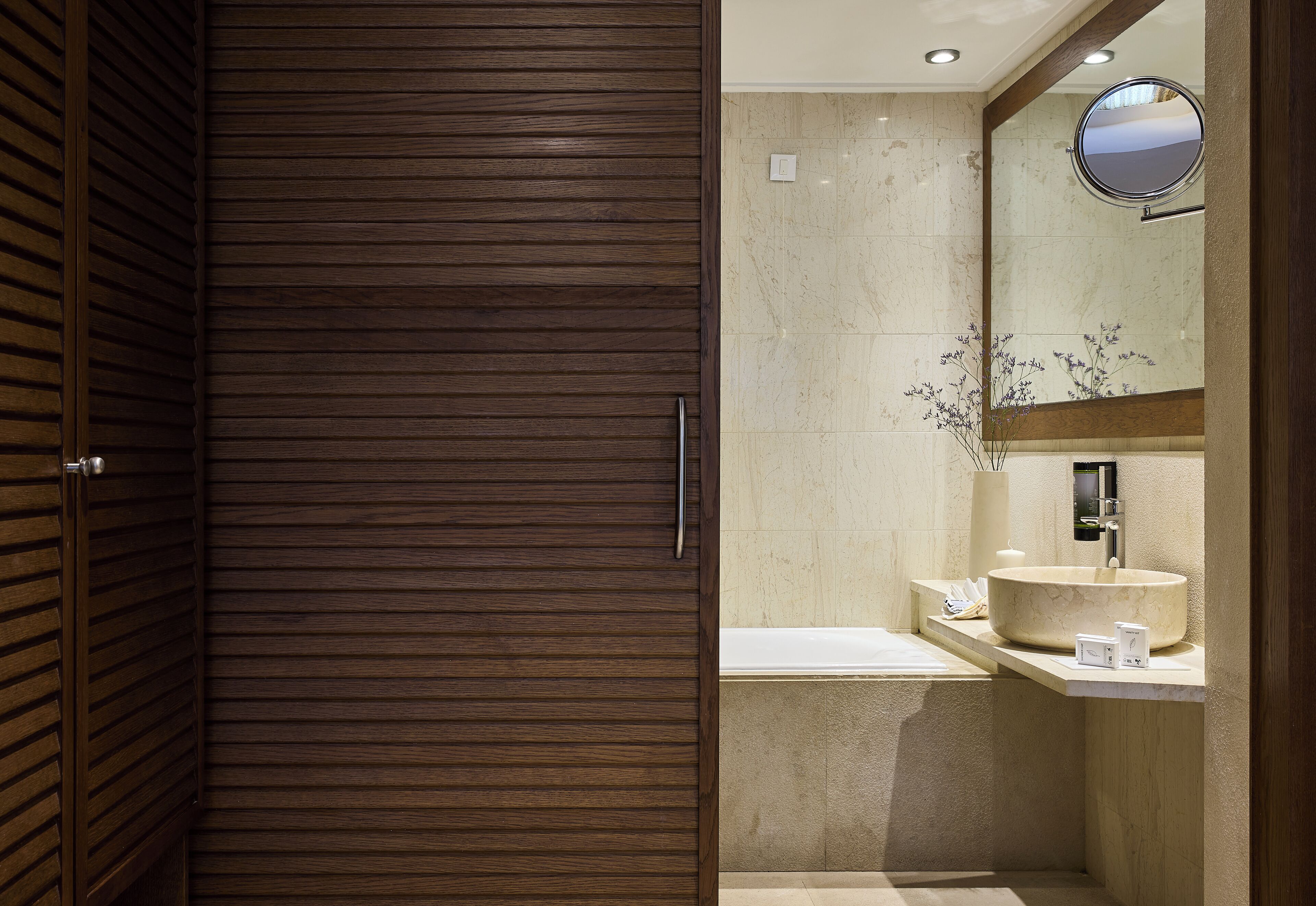 Un baño moderno con puerta corredera de madera, un espejo grande, lavamanos de mármol y una bañera.