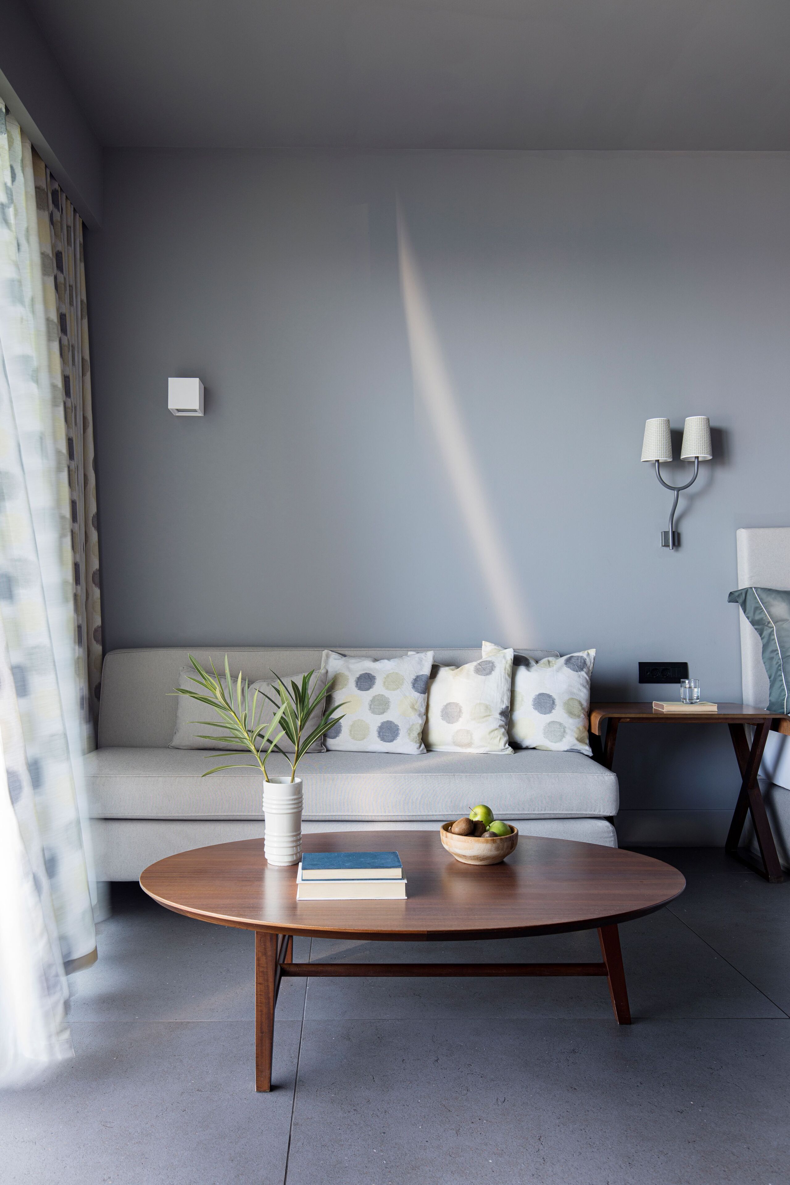 A modern living room with a grey sofa, a round wooden coffee table, a potted plant, and a bowl of fruit.