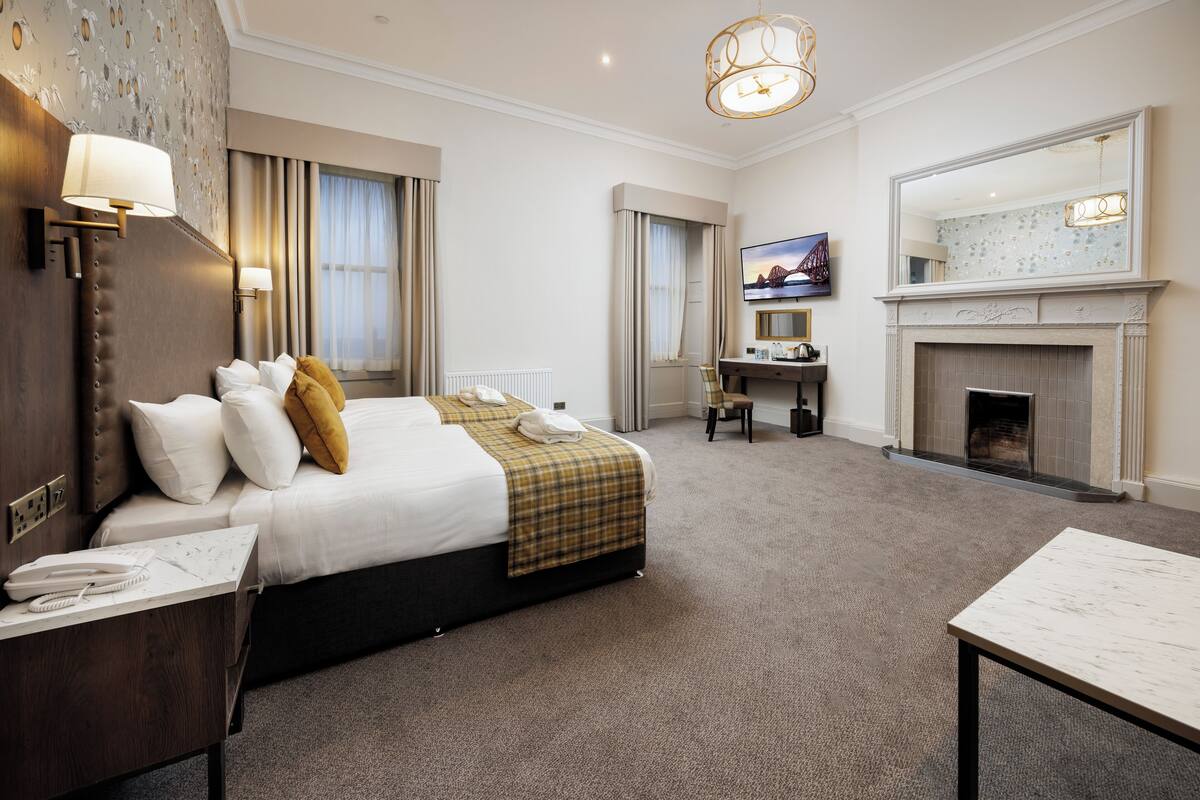 A hotel room with a large bed, a desk, a fireplace, and a television.