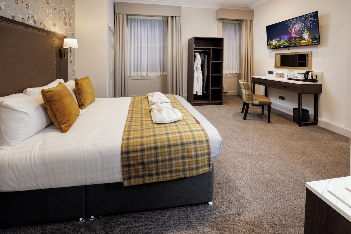 A hotel room with a large bed, a desk, a chair, a wardrobe, and a television.