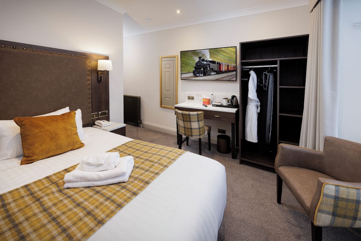 A hotel room with a large bed, a desk, a chair, a wardrobe, and a coat rack.