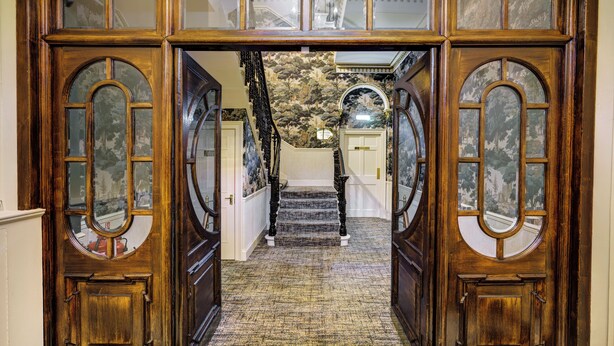 Une entrée imposante avec un sol en marbre, un escalier et des portes en bois dotées de panneaux de verre.