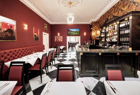 Um restaurante com chão xadrez, assentos estofados vermelhos e um bar com espaço para exibição de vinhos.