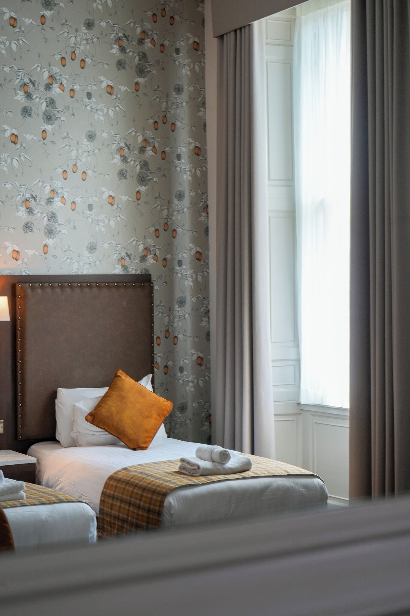 Ein Hotelzimmer mit Bett, Nachttisch, Kopfteil und einem Fenster mit Vorhängen.