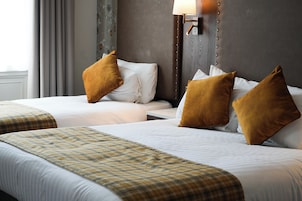 A hotel room with two beds, each with white linens and brown pillows, a plaid throw blanket, and a wooden headboard with a light fixture.