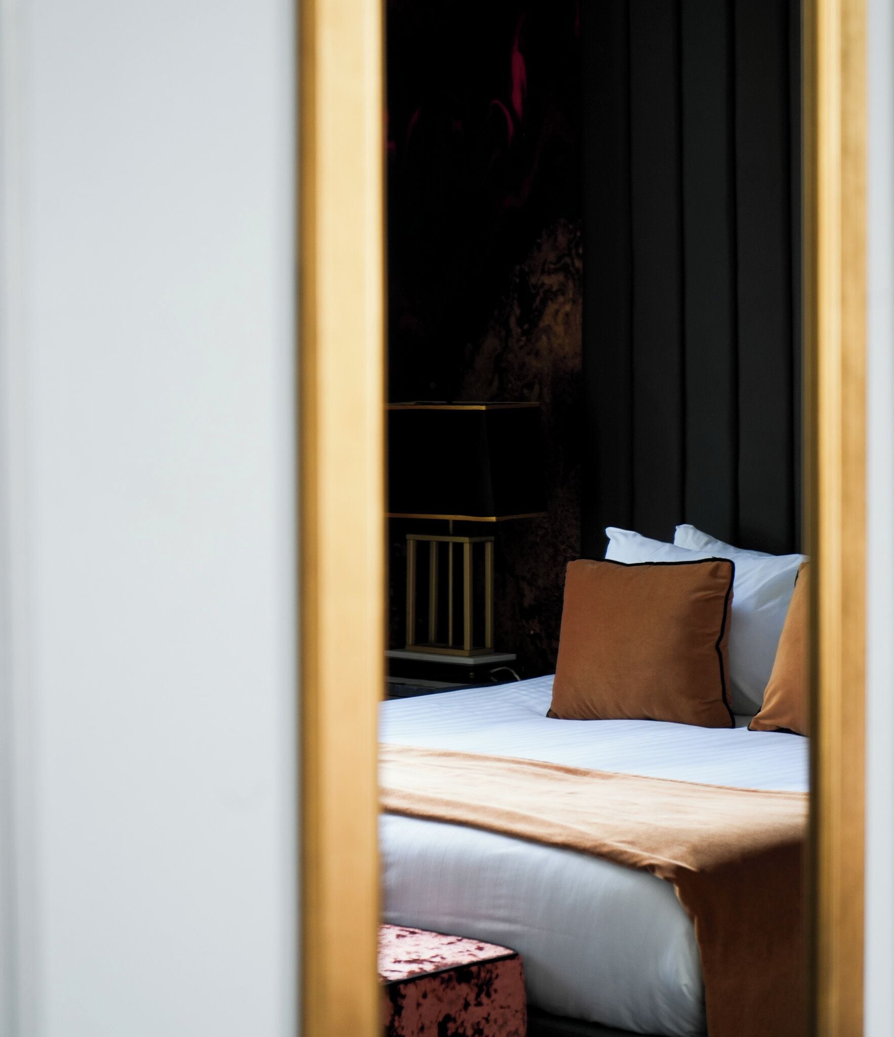 A bed with white bedding and a brown pillow, a small round table, and a dark wall with vertical lines.