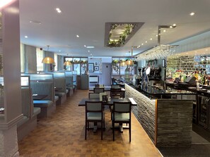 A restaurant with a bar area, seating with high tables, and a view of the street. - Grange Manor (Grangemouth)