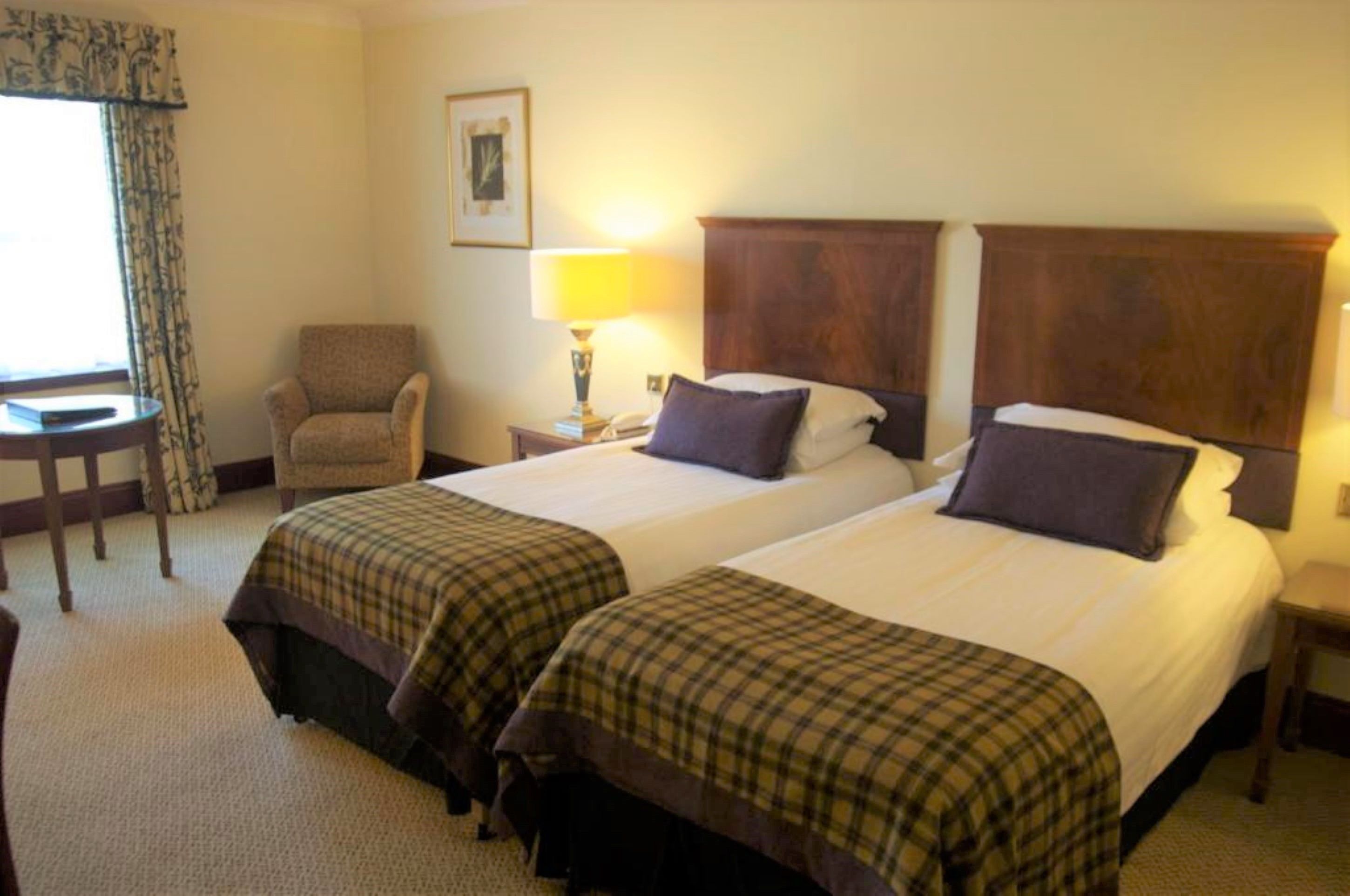 A hotel room with two beds, a chair, a table, and a lamp.
