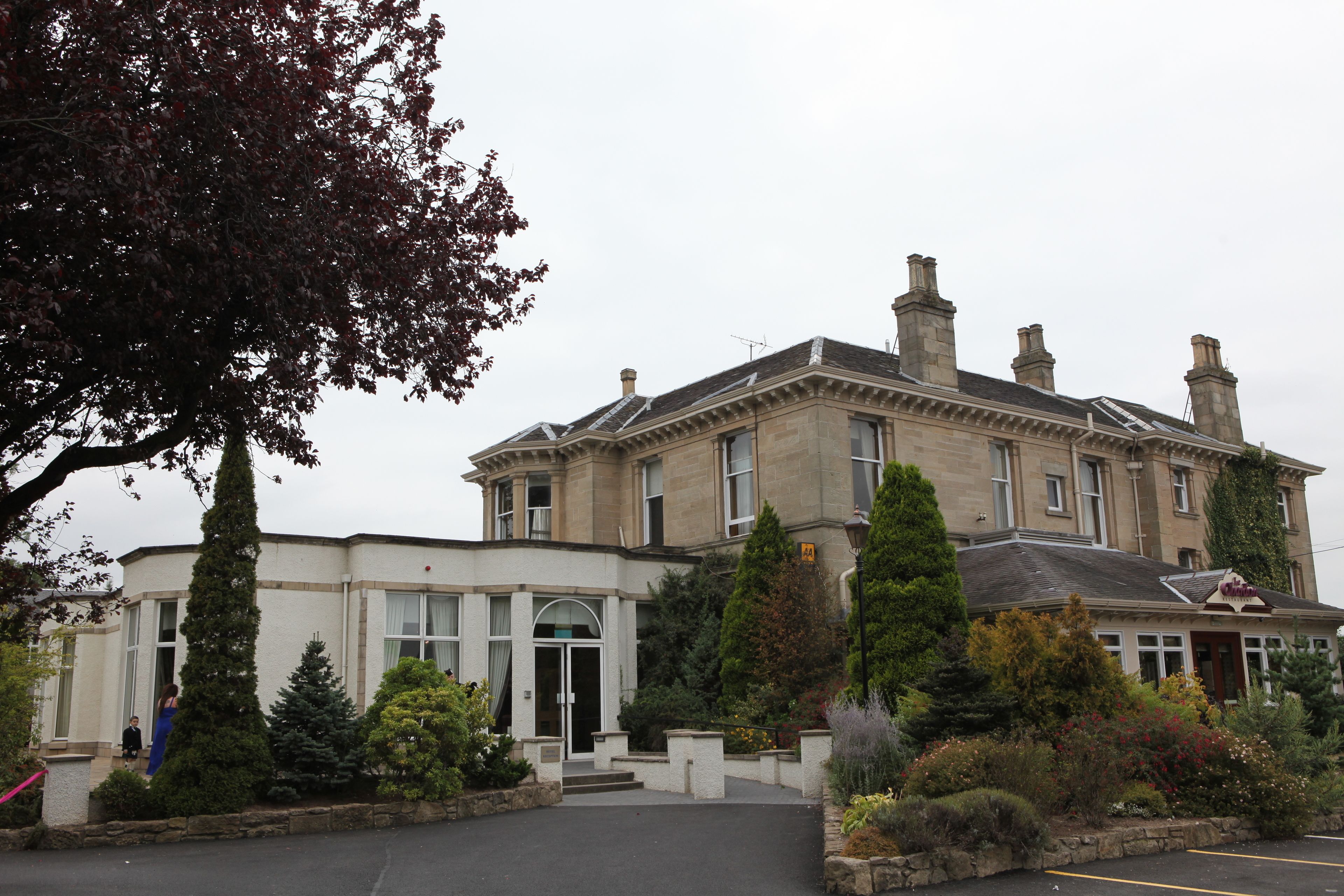 A large, historic building with a symmetrical facade, multiple chimneys, and a central entrance with a glass door.