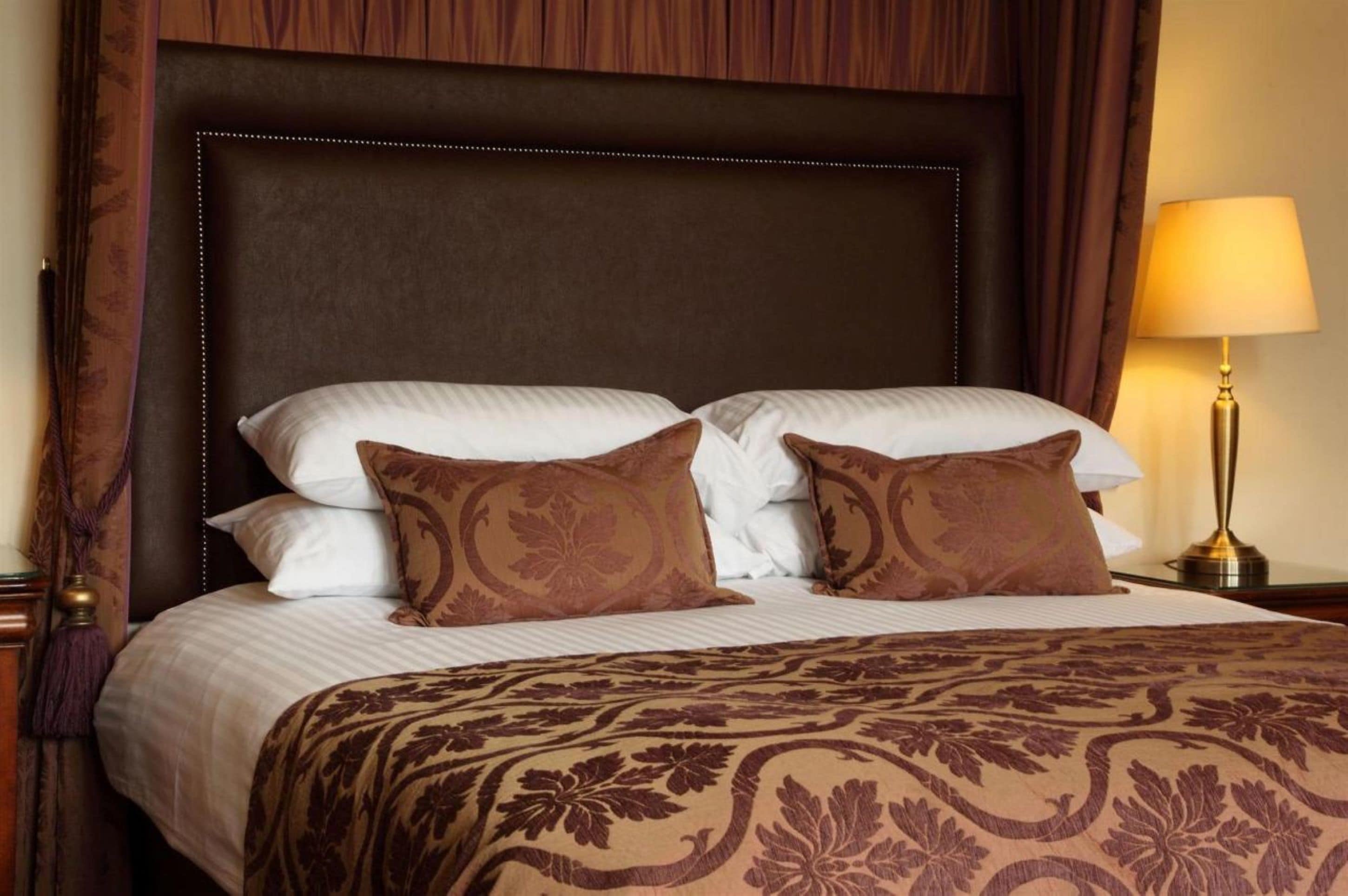 Habitación de hotel con una cama grande, cabecera de madera y una lámpara de noche.