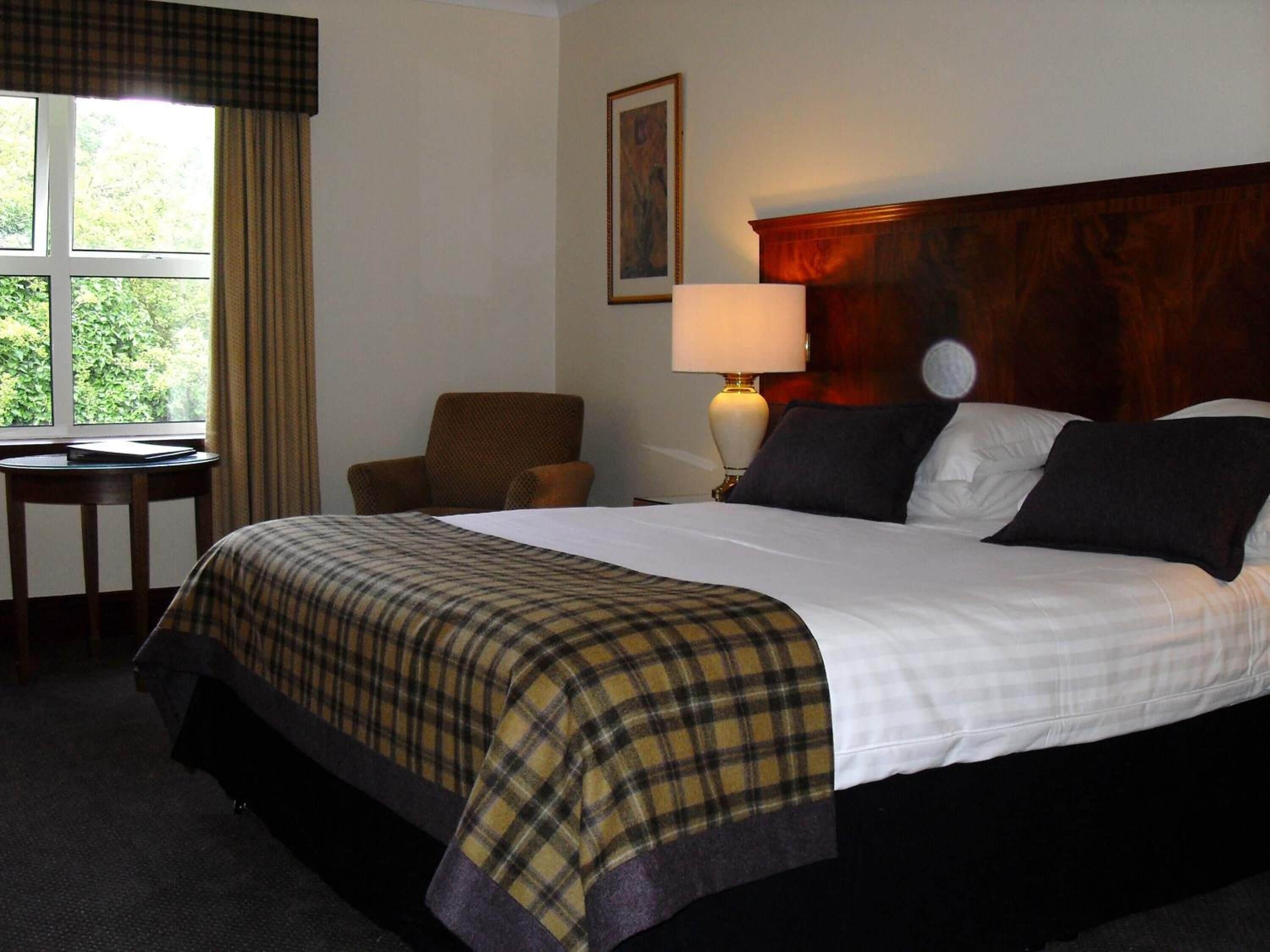 A hotel room with a large bed, a chair, a desk, and a window with curtains.