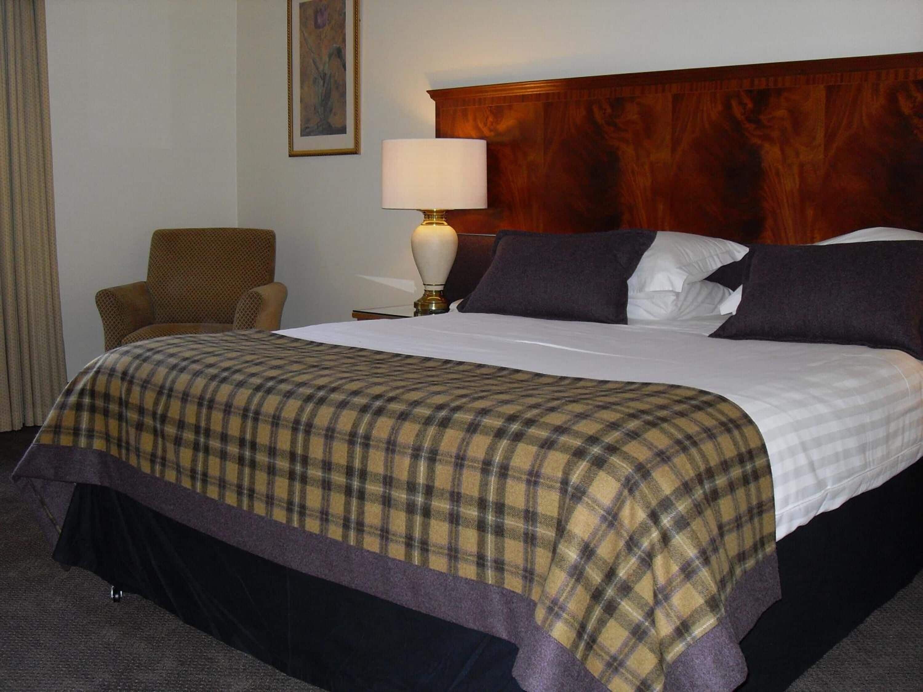 A hotel room with a large bed, a wooden headboard, a chair, a lamp, and a painting on the wall.