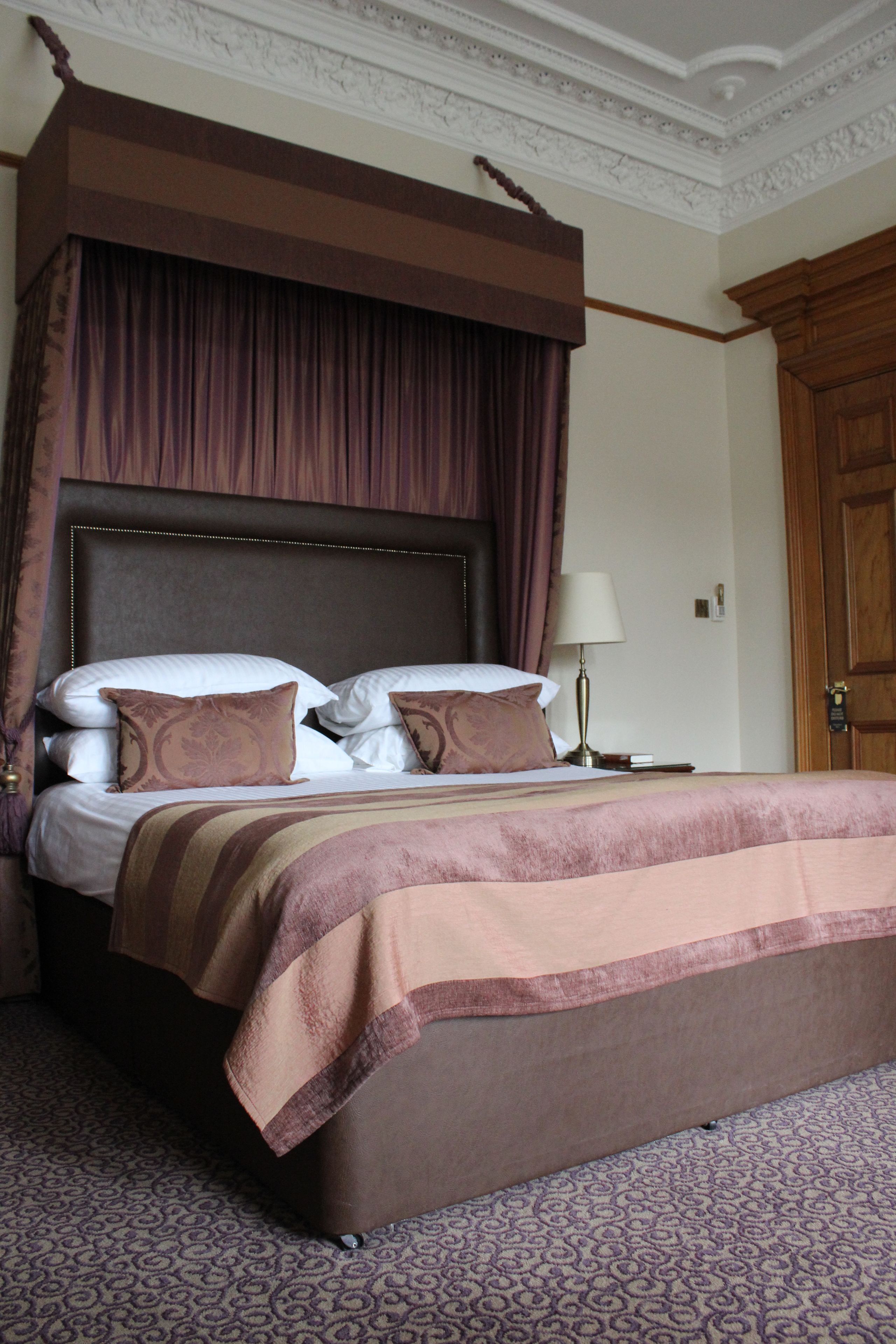 A hotel room with a large bed, a wooden headboard, a nightstand with a lamp, and a door.