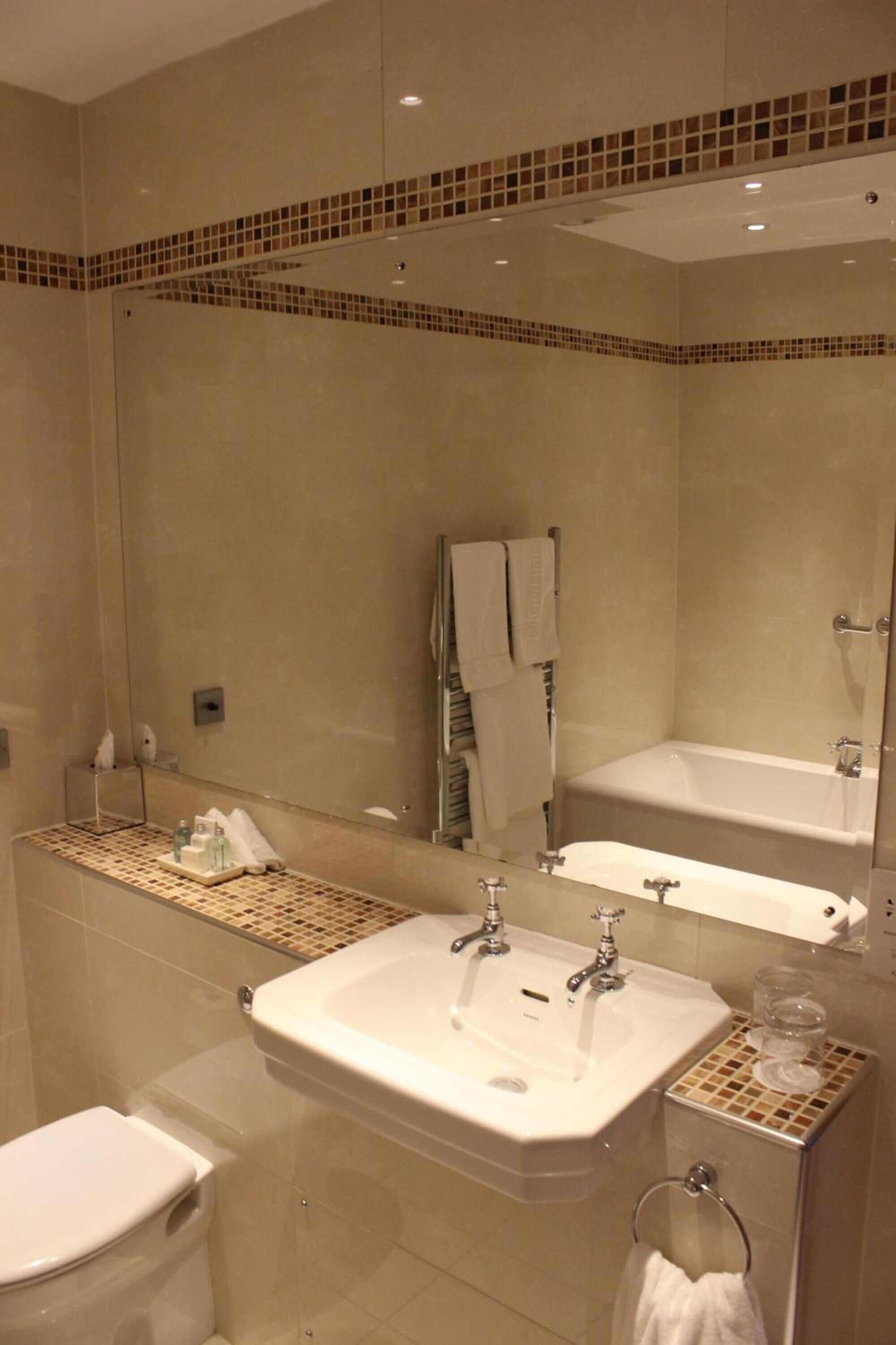 A modern bathroom with a large mirror, two sinks, a bathtub, and a toilet.