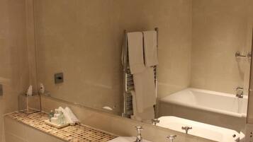 A modern bathroom with a large mirror, two sinks, a bathtub, and a toilet.