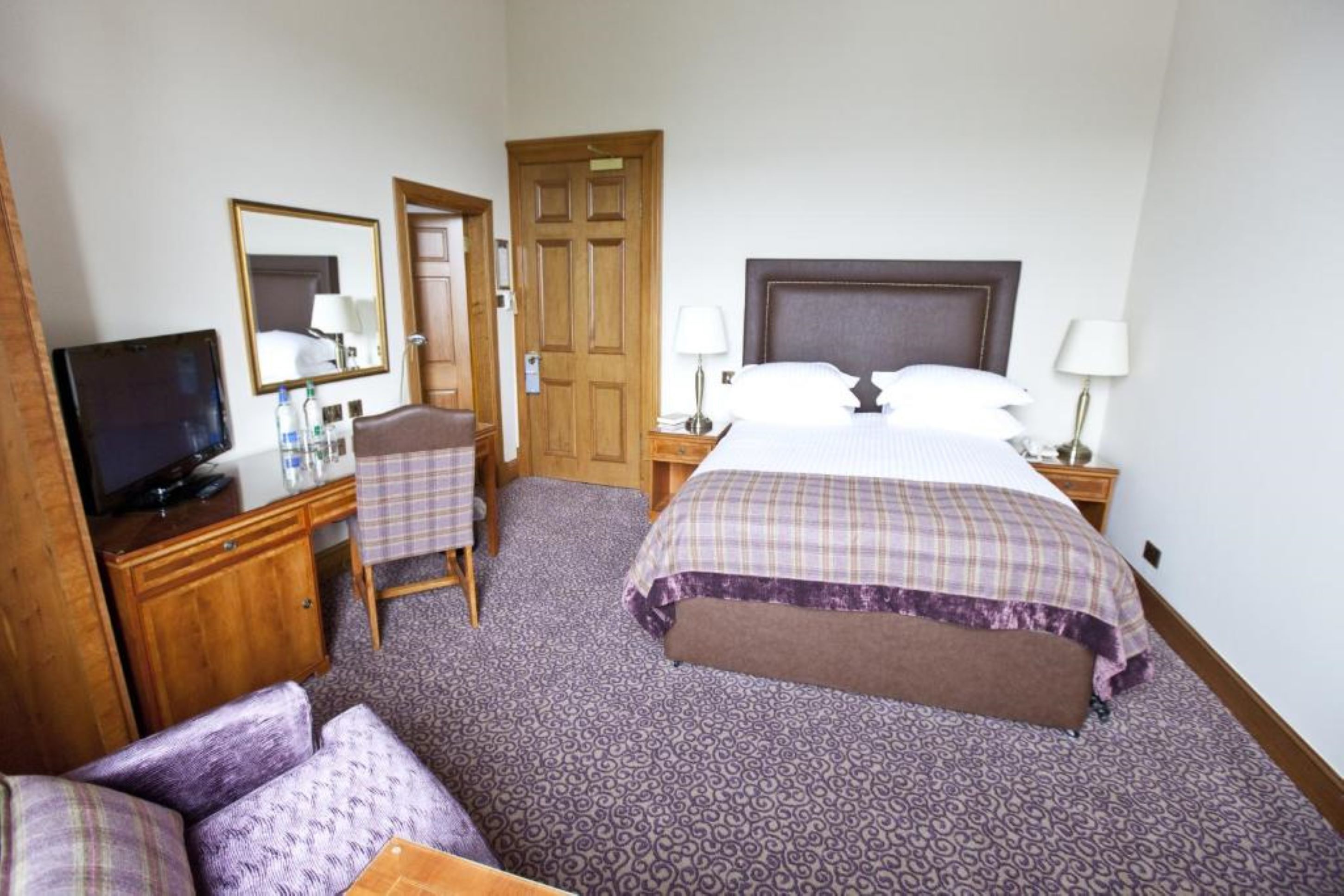 A hotel room with a bed, a desk with a computer, a chair, and a television.