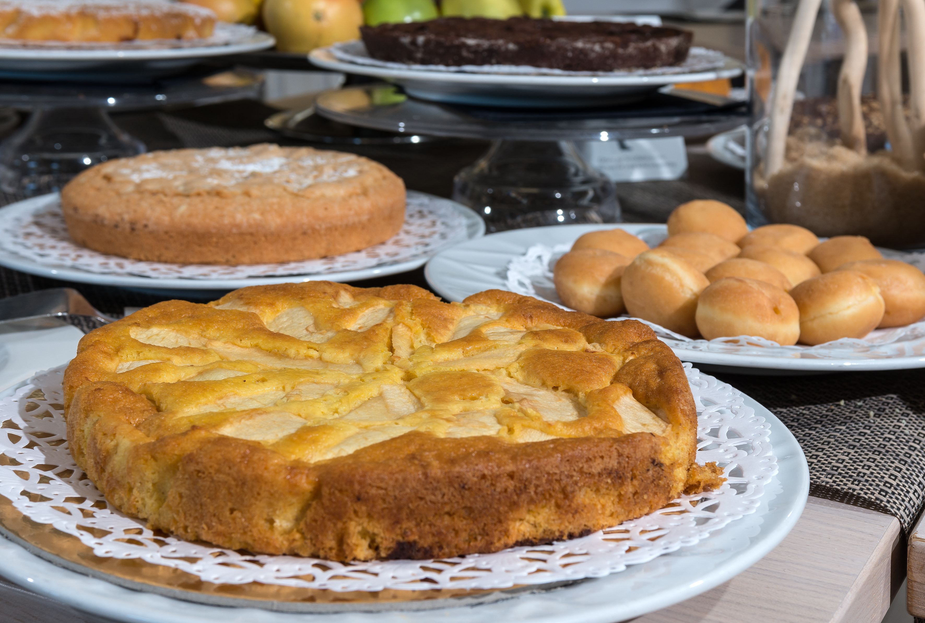 Una mesa con diferentes productos de repostería, incluyendo un pastel con fruta, panecillos y otras pastas.