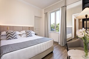 Siististi järjestetty hotellihuone, jossa on suuri sänky, oleskelualue pöydällä ja ikkuna, jossa on verhot.
