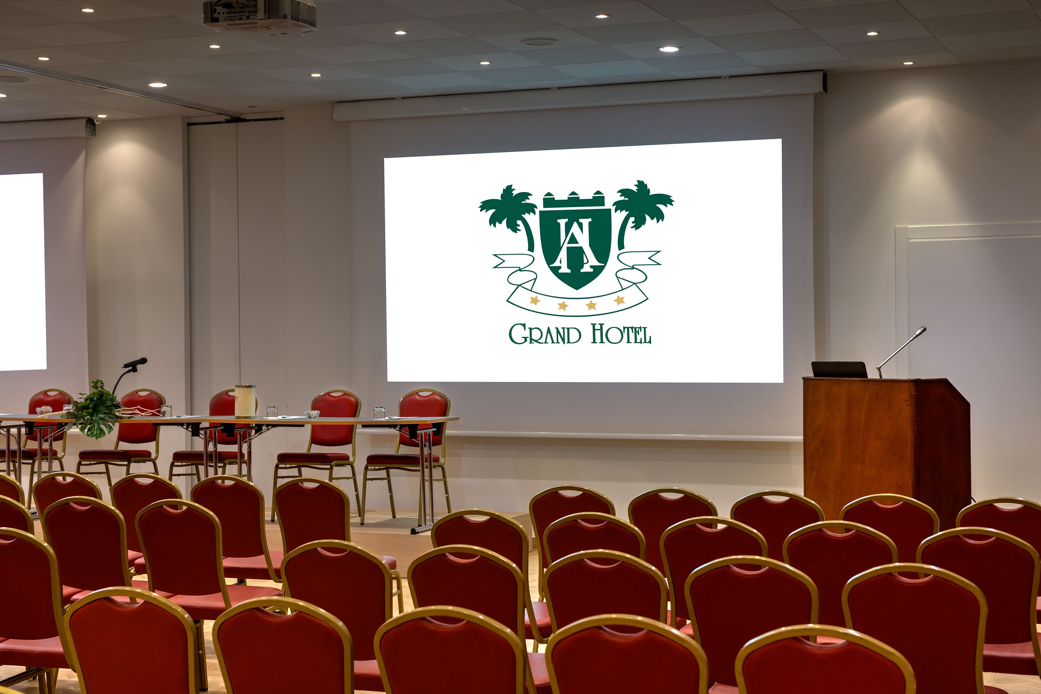 A conference room with red chairs, a podium, and a screen displaying a hotel logo.