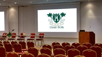 A conference room with red chairs, a podium, and a screen displaying a hotel logo.