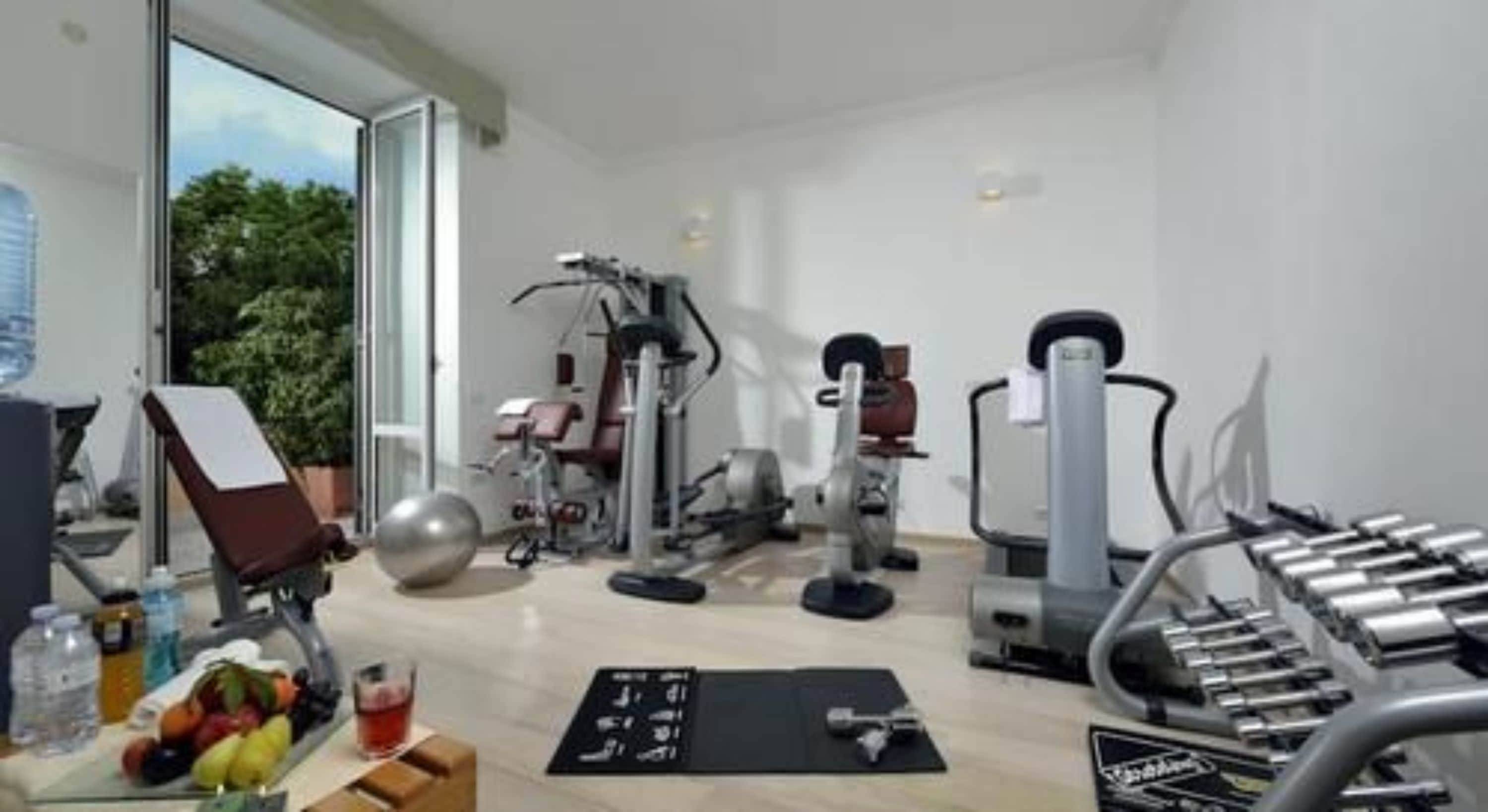 Ein Heimfitnessraum mit unterschiedlichen Trainingsgeräten, einer Yogamatte und einer Obstschale.