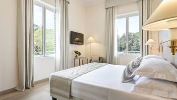 Un cuarto de hotel con una cama grande, dos lámparas de noche, una mesita con una planta y vistas a la vegetación a través de las ventanas.