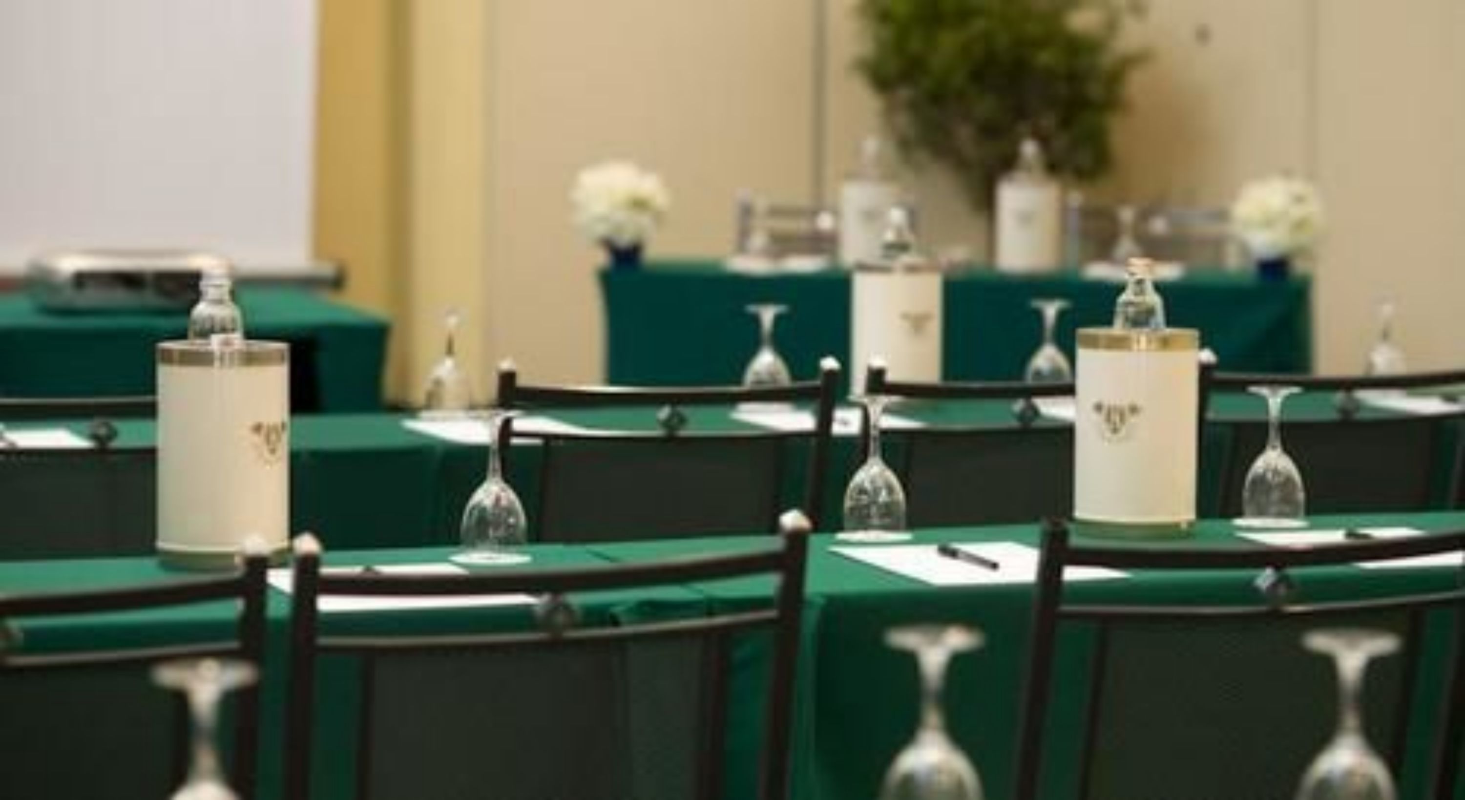 Rows of tables with green tablecloths, each with a clear glass and a white candle holder.
