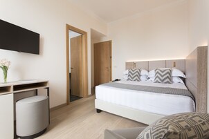 Moderni hotellihuone, jossa on sänky, yöpöytä ja seinälle asennettu taulutelevisio.