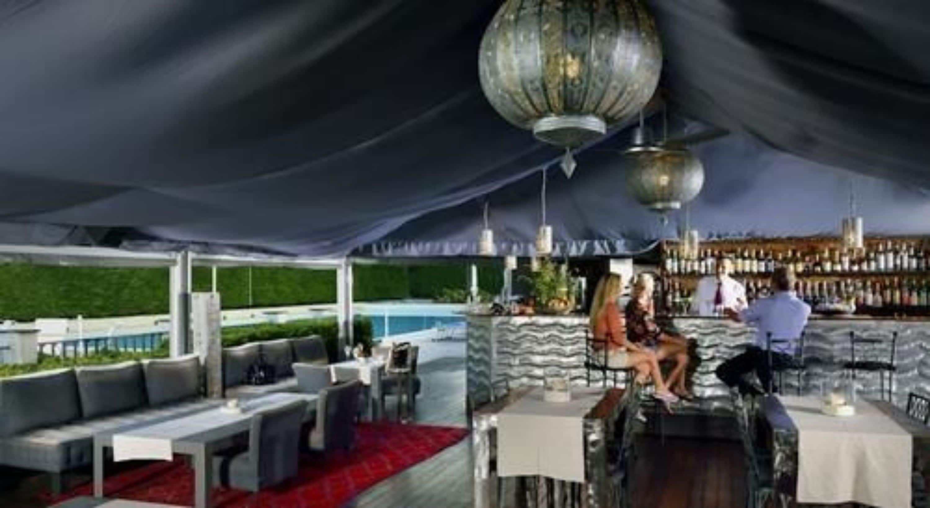 An outdoor bar area with a pool in the background, covered by a large tent.