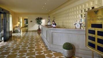 A hotel lobby with a check-in counter, a reception desk, and a tiled floor.