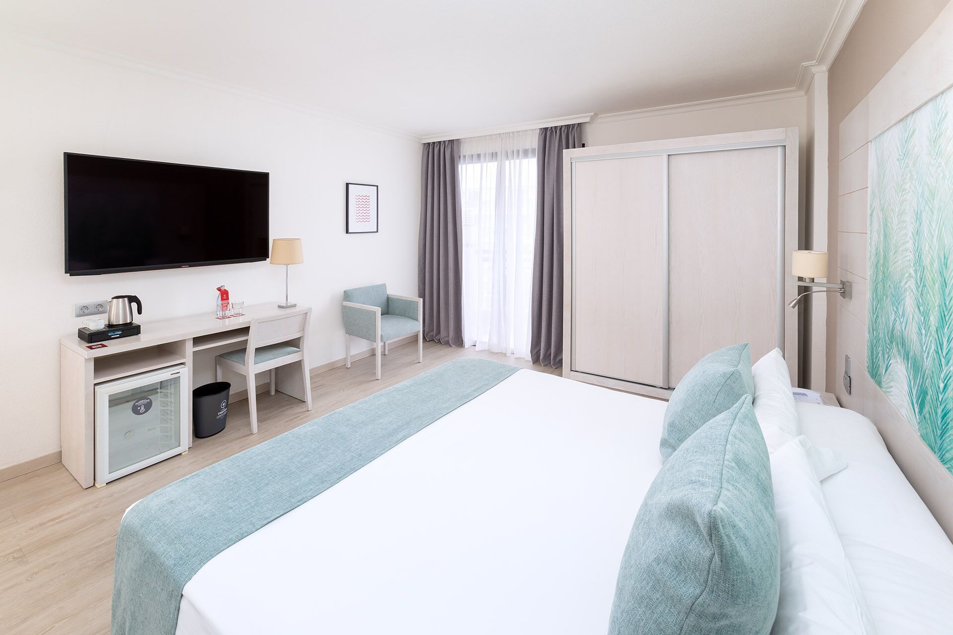Una habitación de hotel con cama, escritorio con silla, televisor, máquina de café y armario.