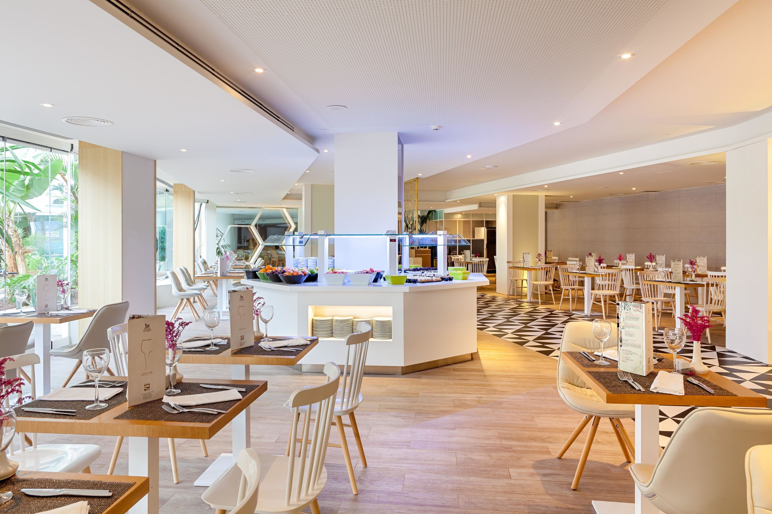 A modern dining area with white chairs and tables, a central buffet, and a checkered floor pattern.